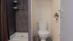 Een badkamer met een douche, toilet en een klein wastafeltje.