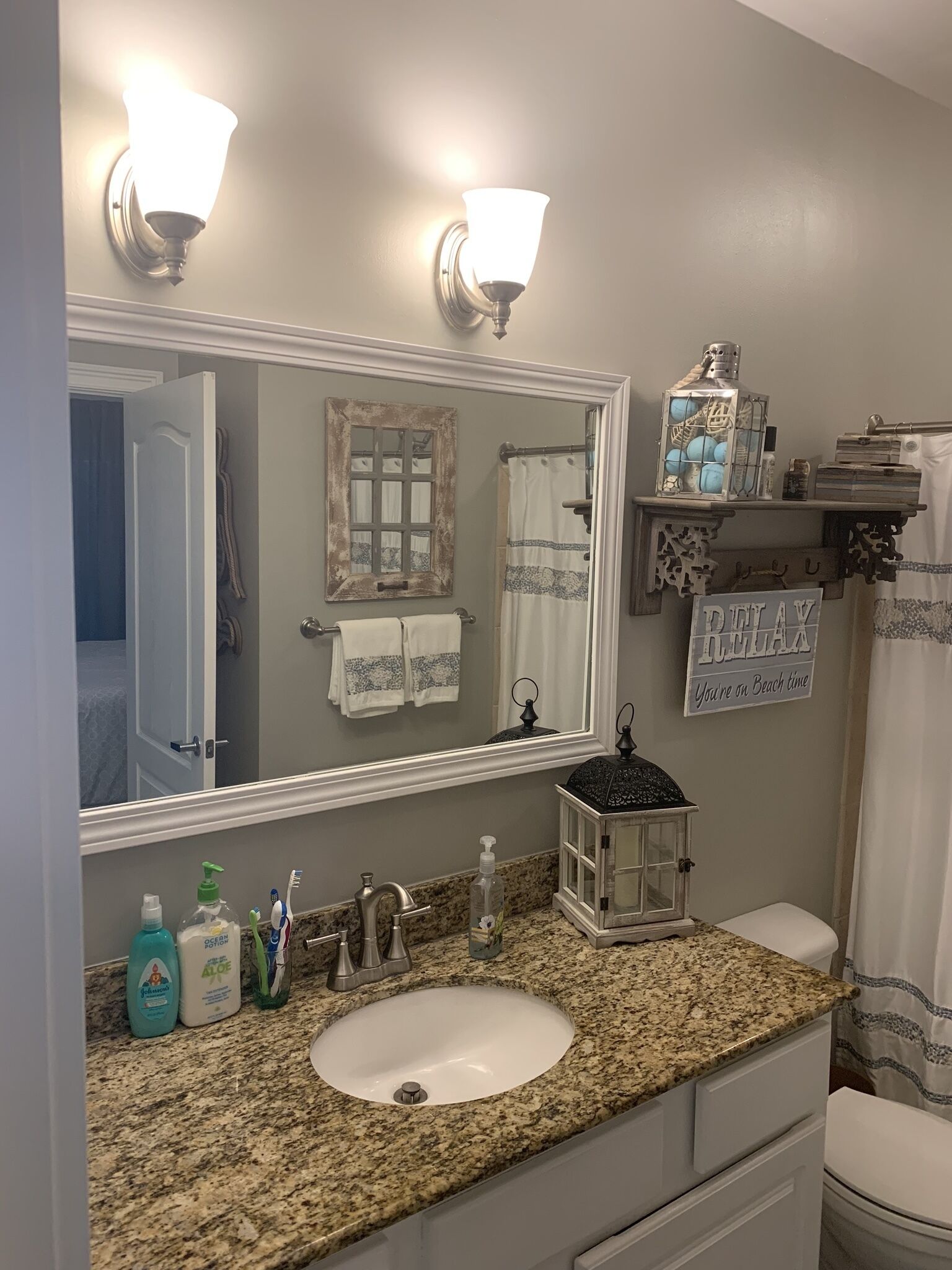 Une salle de bain avec un comptoir en granit, un lavabo blanc, un grand miroir et un rideau de douche.