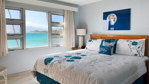 Une chambre avec un grand lit, un ventilateur de plafond, une fenêtre donnant sur l’océan et une lampe fixée au mur.