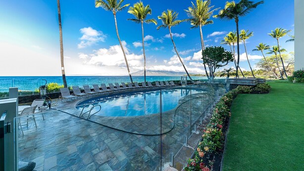 Un espace aménagé au bord de la piscine, avec des chaises longues, des palmiers et une vue sur l’océan.