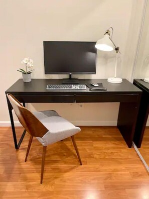Un espacio de trabajo moderno con un escritorio de madera, una computadora, un teclado, un ratón, una lámpara y una silla.