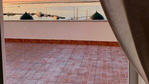 Uitzicht vanaf een balkon met tegels, op een rustige zee en boten.