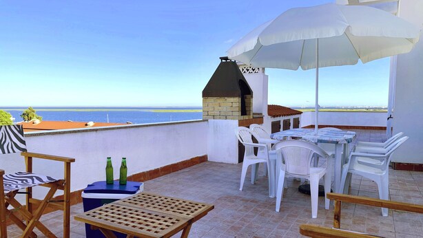 Een terras met een tafel en stoelen, een barbecue en uitzicht op zee.