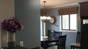 Een keuken met een granieten aanrecht, een vaas met bloemen, een eettafel met stoelen, een kroonluchter en een klok aan de muur.