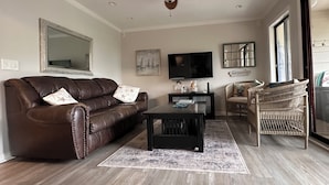 Een woonkamer met een bruine leren bank, een zwarte salontafel, een plafondventilator, een flatscreen-televisie en een rieten fauteuil.