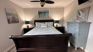 Een slaapkamer met een donker houten bed, een plafondventilator, twee nachtkastjes met lampen, een dressoir en kunstwerken aan de muur.