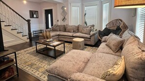 Ein Wohnzimmer mit einem Ecksofa, einem Couchtisch, einer Stehlampe, einem Deckenventilator und einer Treppe.
