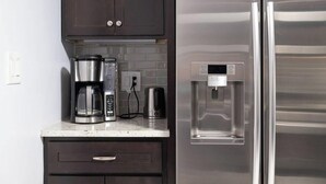Eine Küche mit dunklen Schränken, einem Edelstahlkühlschrank, einer Kaffeemaschine und einem Wasserspender.