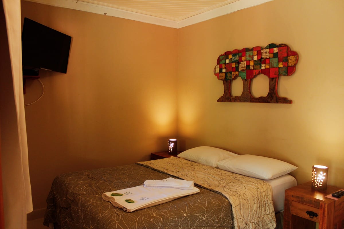 Habitación de hotel con cama, televisor de pared, obra de arte con un árbol decorativo y lámparas de noche.
