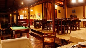 A billiards room with multiple tables and chairs, wooden beams on the ceiling, and a green pool table in the foreground. - Pousada Araucária (São Luiz do Paraitinga)