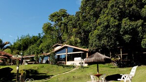 A pool area with a clear blue pool, a thatched umbrella, and white lounge chairs. - Pousada Araucária (São Luiz do Paraitinga)
