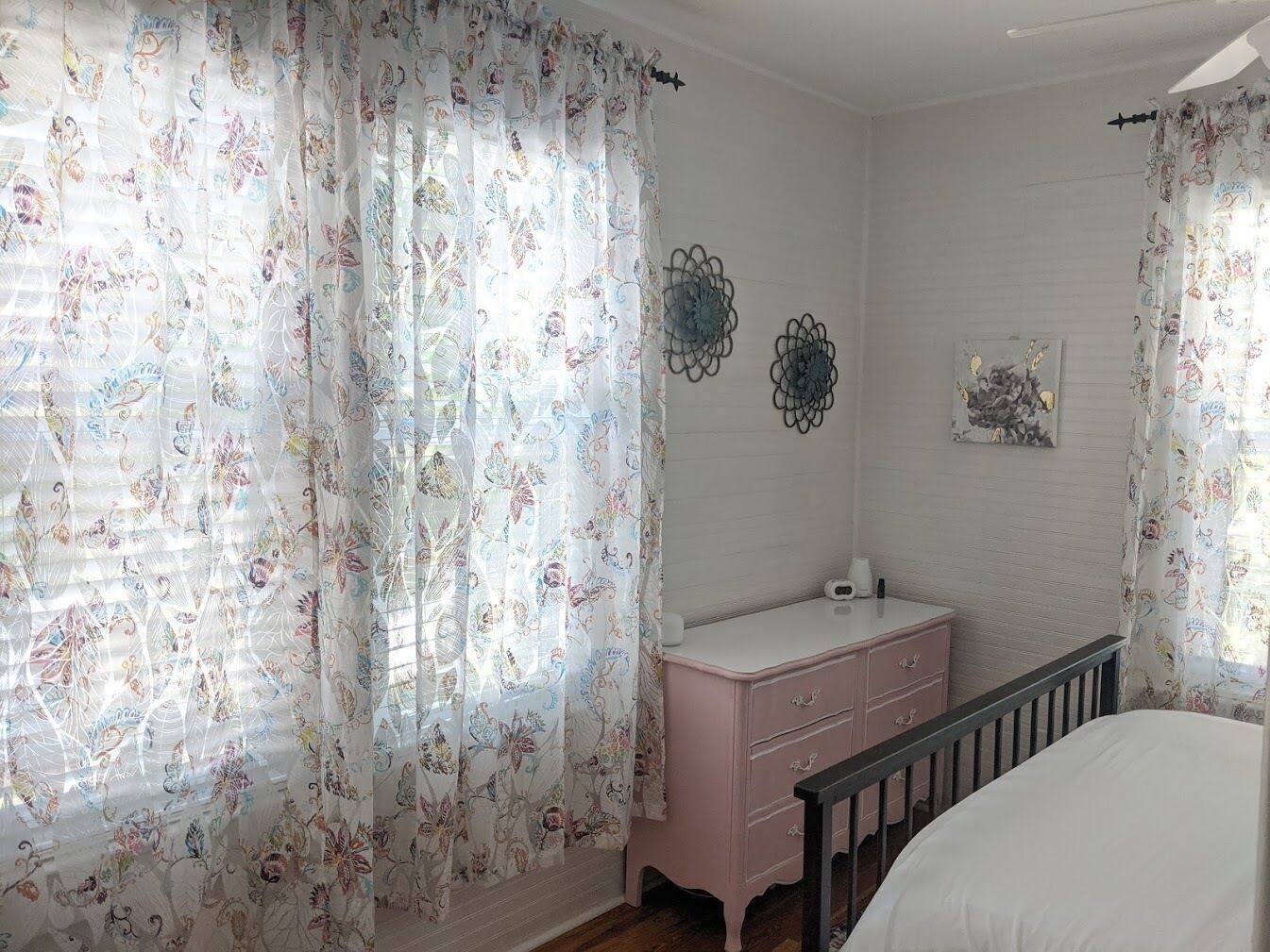Ein Schlafzimmer mit blumigen Vorhängen, einem rosa Schminktisch, einem Bett und Wanddekorationen.