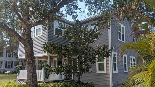 A two-story residential building with a covered front porch, a tree in front, and a well-maintained lawn. - This Suite Old House (Cocoa)