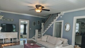 A living room with a sofa, coffee table, and a television on a white cabinet. - This Suite Old House (Cocoa)