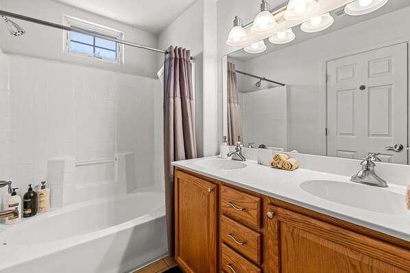 Une salle de bain moderne avec une baignoire, deux lavabos, des meubles en bois et un grand miroir avec éclairage intégré.