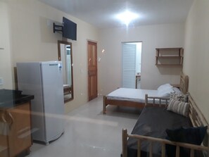A small, well-lit room with a bed, a desk, a refrigerator, and a television mounted on the wall.