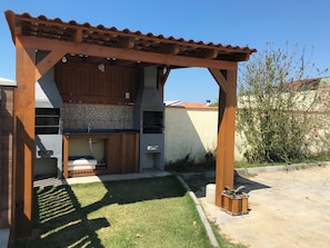 A wooden pergola with a tiled roof, a built-in grill, and a small sink.