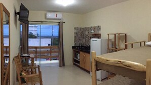 Una habitación pequeña y acogedora con una mesa de madera, una silla, kitchenette y una puerta corrediza de vidrio que da a un balcón.