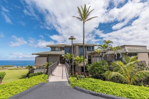 A modern two-story house with a covered walkway leading to the entrance, surrounded by lush greenery and a view of the ocean. - Kapalua Bay Villa 34B3 Corner Ocean View Villa (Lahaina)