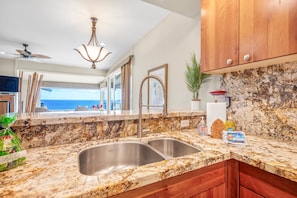 A kitchen with granite countertops, stainless steel sink, wooden cabinets, and a view of the ocean. - Kapalua Bay Villa 34B3 Corner Ocean View Villa (Lahaina)