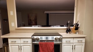 La cuisine est équipée d’une cuisinière, d’un four et d’un four à micro-ondes en acier inoxydable. Une serviette rouge est accrochée à la porte du four. Les meubles de cuisine sont blancs et le plan de travail est de couleur beige.