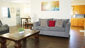 Ein Wohnzimmer mit grauem Sofa, gemusterten Kissen, einem Holztisch und einem Bild an der Wand.