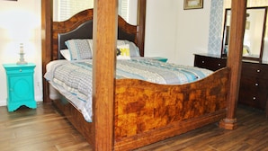 Ein Bett mit Baldachin, dessen Kopfteil und Fußteil aus Holz gefertigt sind, ein Türkis-Nachttisch und eine Holzkommode mit Schubladen.