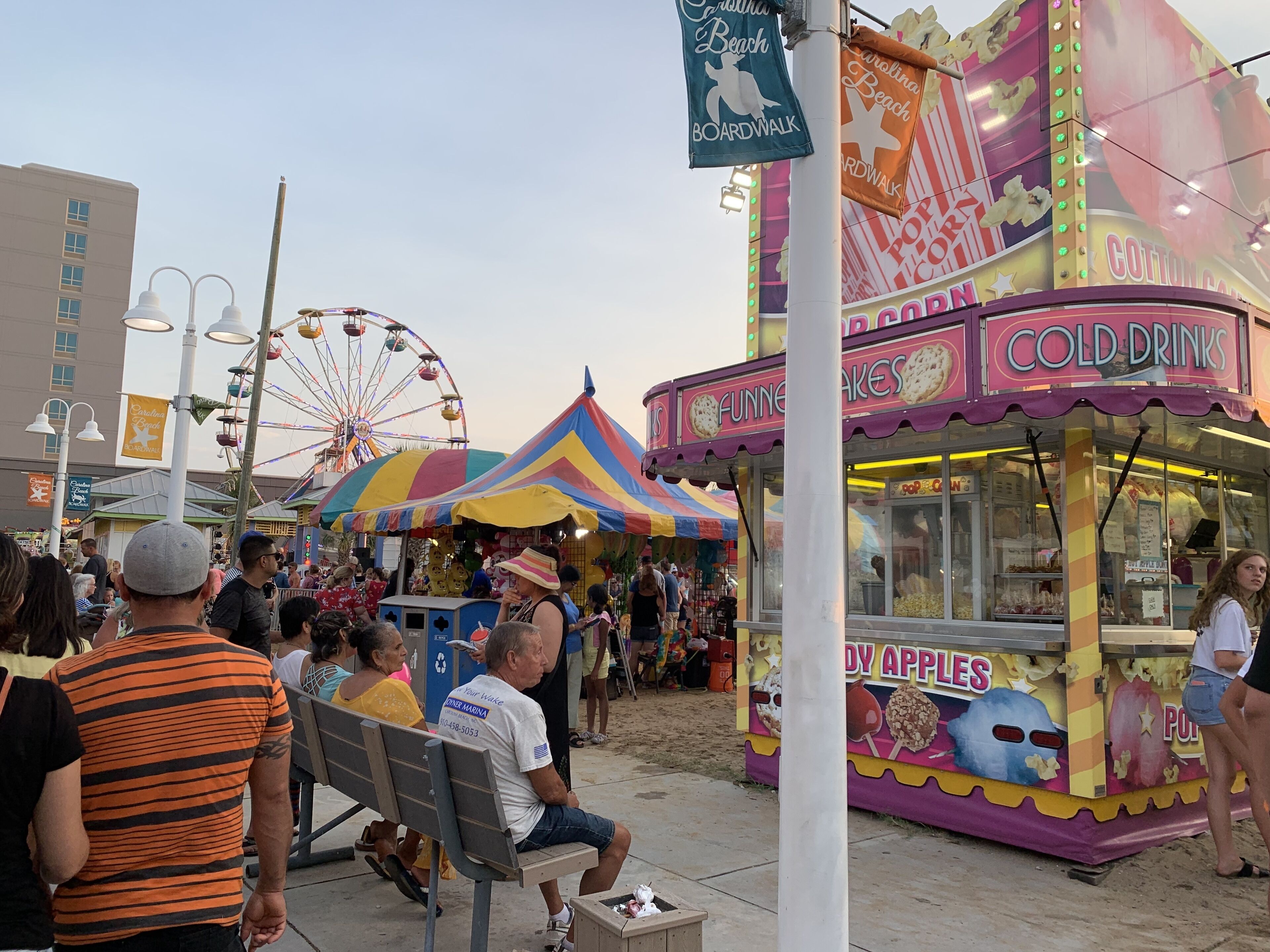 Une promenade en bord de mer avec une grande roue, un stand de restauration et un espace abrité par une tente.