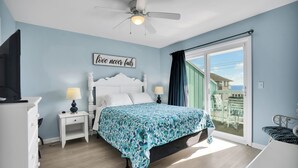 Une chambre à coucher comprenant un lit, une table de chevet, une commode, un ventilateur de plafond et une fenêtre donnant sur un paysage agréable.