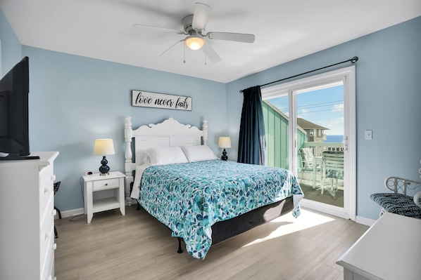 Une chambre à coucher comprenant un lit, une table de chevet, une commode, un ventilateur de plafond et une fenêtre donnant sur un paysage agréable.