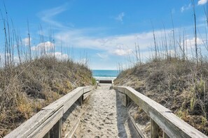 Un sentier de sable bordé de rambardes en bois qui mène à l’océan.