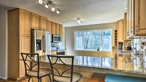 A kitchen with wooden cabinets, stainless steel appliances, a granite countertop, and a window with a view of trees. - Charming Kelso Home w/ Proximity to Cowlitz River! (Kelso)