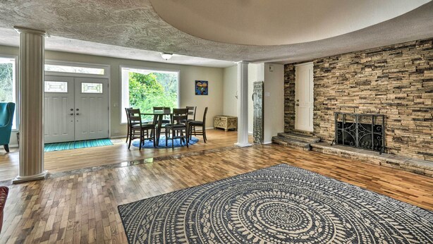 A spacious living room with hardwood flooring, a large rug, a stone fireplace, and a dining area with chairs and a table. - Charming Kelso Home w/ Proximity to Cowlitz River! (Kelso)