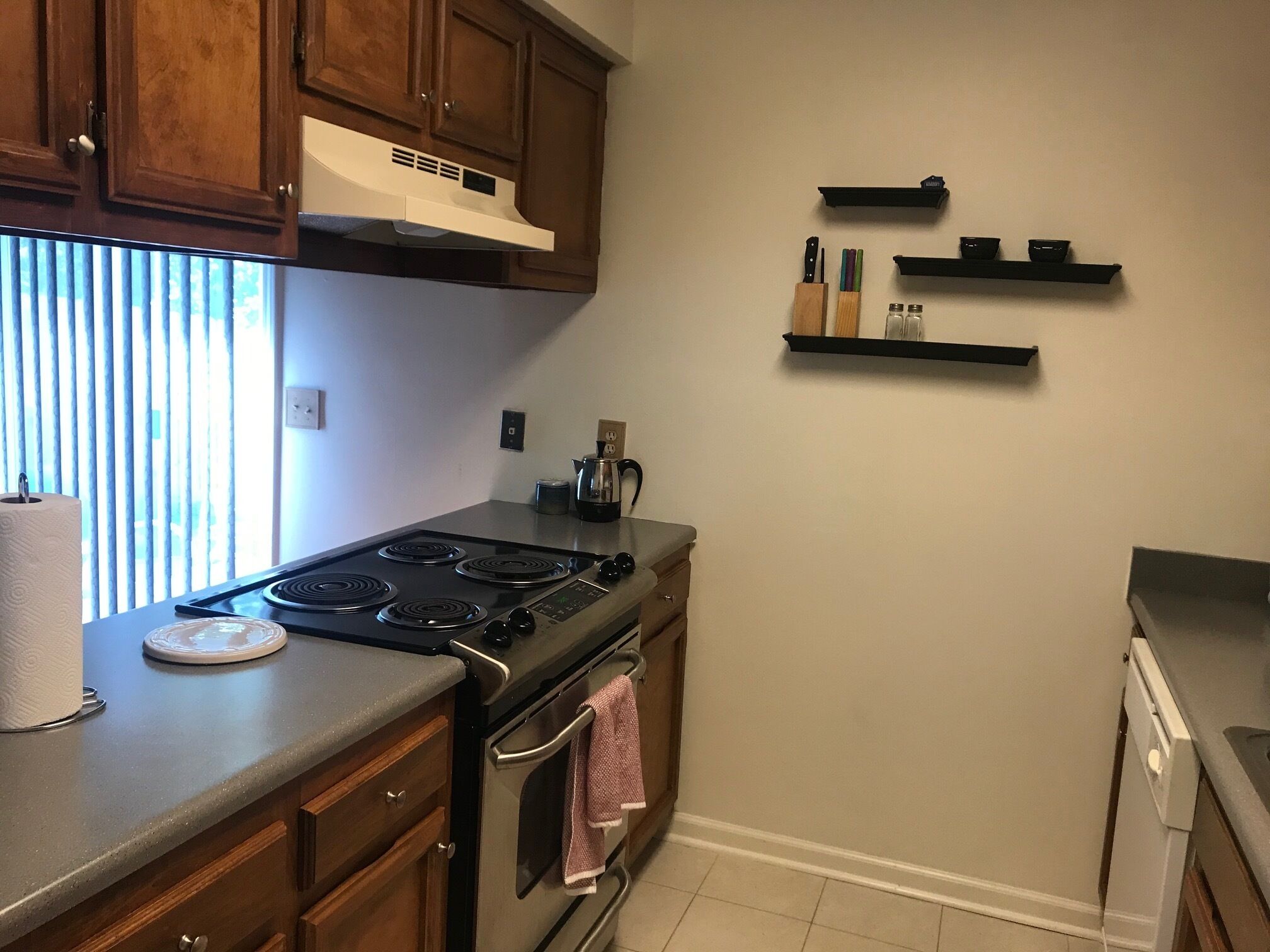 A kitchen with wooden cabinets, a stove, and a countertop. There are three black shelves on the wall.