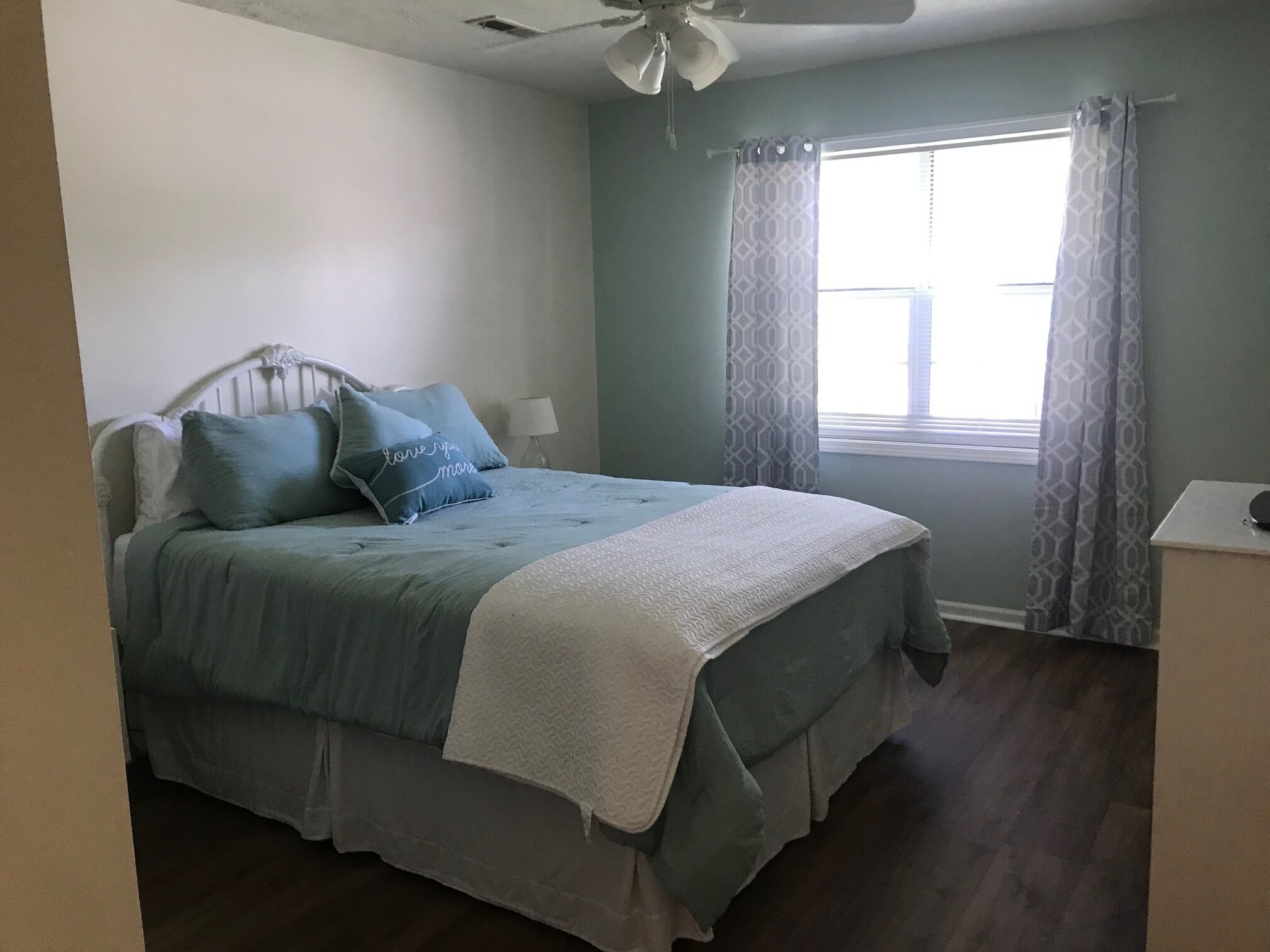 A bedroom with a bed, a ceiling fan, a window with curtains, and a bedside table.