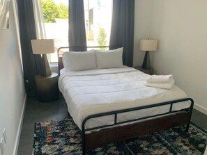 A neatly made bed with white linens, two bedside lamps, and a patterned rug on a carpeted floor.