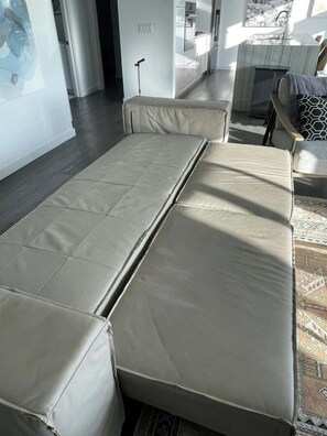 A modern bedroom with a bed, a chair, and a view of the kitchen.