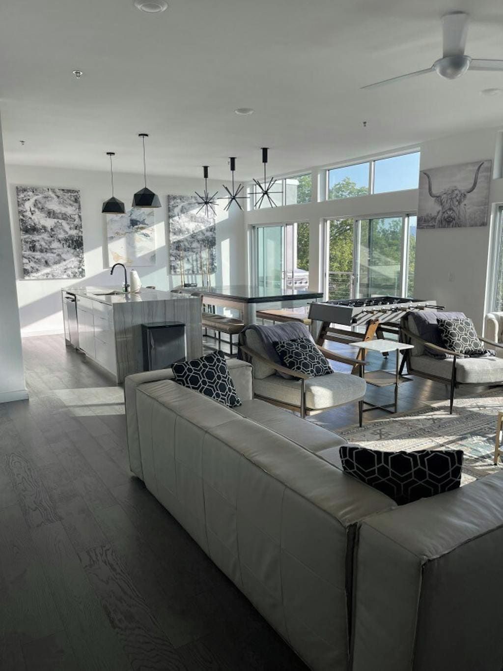 A spacious living area with a large sofa, a coffee table, and a fireplace. There are multiple seating options and a kitchen area visible in the background.