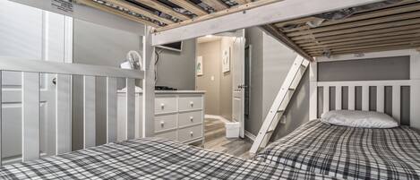 Una habitación con dos camas, un aparador y una escalera que sube a un nivel superior.