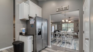 A kitchen with white cabinets, a stainless steel refrigerator, and a trash bin. There is a sign that reads "welcome to SUGAR ISLE". - Private Pool! Walk to Beach! 3 Kings & Quad Bunk! (Miramar Beach)