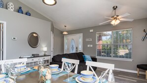 A dining area with a table set for four, a ceiling fan, and a view of the outdoors through a window. - Private Pool! Walk to Beach! 3 Kings & Quad Bunk! (Miramar Beach)