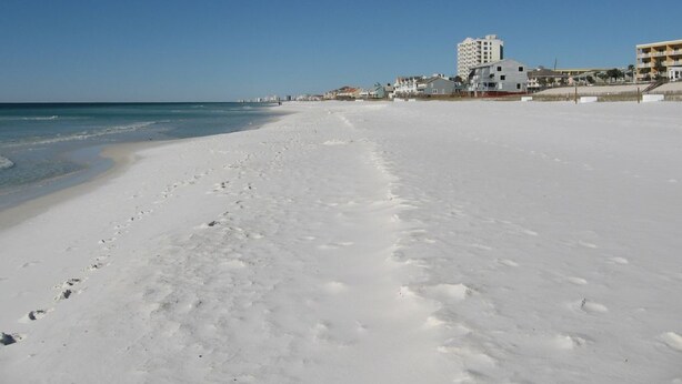 A wide, snow-covered beach with footprints leading to the water, buildings in the background, and a clear blue sky. - Private Pool! Walk to Beach! 3 Kings & Quad Bunk! (Miramar Beach)