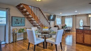 Un coin repas avec un escalier en bois, une table dressée pour quatre personnes et une cuisine en arrière-plan.