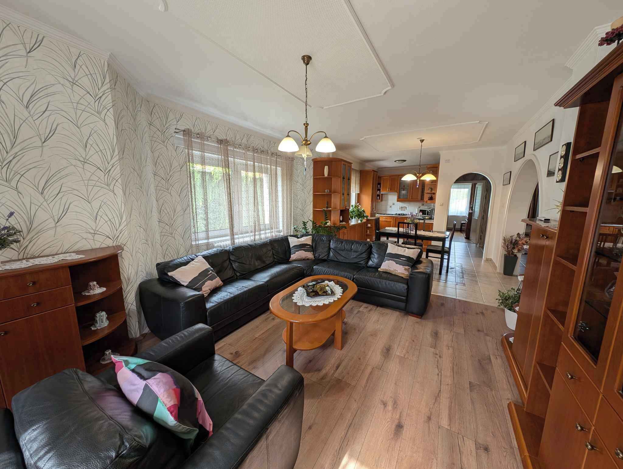 A spacious living room with a sectional sofa, a wooden coffee table, and a kitchen in the background.