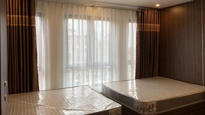 Une chambre d’hôtel avec deux lits simples, une grande fenêtre avec des rideaux légers et une vue sur le paysage urbain.