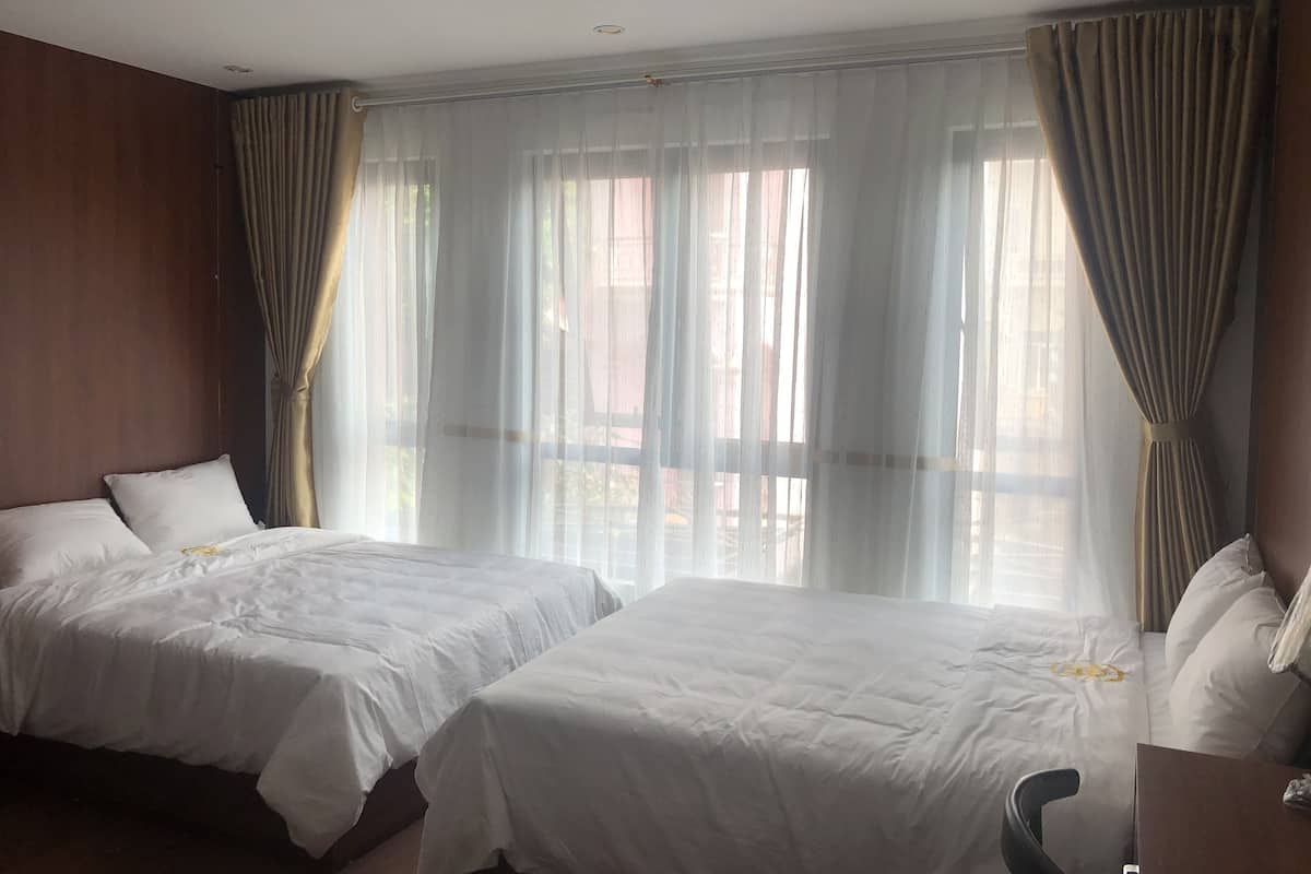 Habitación de hotel con dos camas, cabecera de madera, cortinas translúcidas y vistas al exterior.