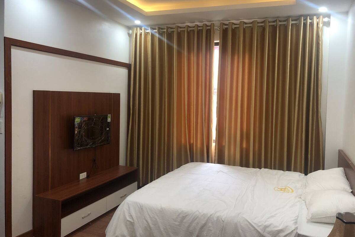 Una habitación de hotel con una cama, un televisor fijado a un panel de madera y una cortina.