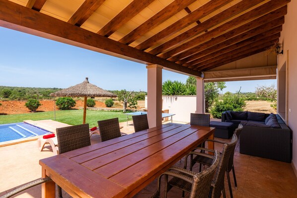 An outdoor patio with a wooden table and chairs, a pool, and a view of the landscape.