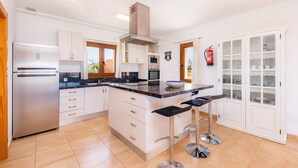 A modern kitchen with a central island, stainless steel appliances, and a fire extinguisher on the wall. - Beautiful Country House "Sa Xorca" with Pool, Air Conditioning, and Wi-Fi (Santanyí)