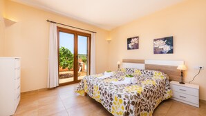 A bedroom with a bed, a nightstand, a lamp, a window with curtains, and a view of greenery outside. - Beautiful Country House "Sa Xorca" with Pool, Air Conditioning, and Wi-Fi (Santanyí)